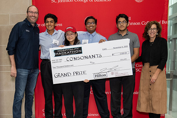 six people standing in front of a red SC Johnson College of Business backdrop holding a large novelty check. 