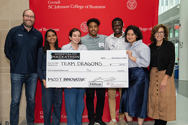 seven people standing in front of a red SC Johnson College of Business backdrop holding a large novelty check. 
