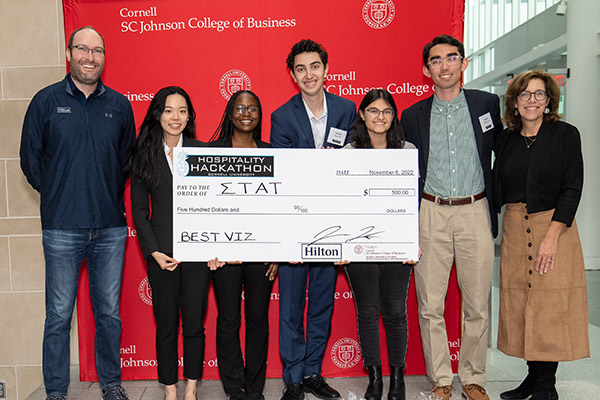 seven people standing in front of a red SC Johnson College of Business backdrop holding a large novelty check. 