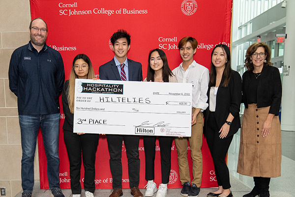 seven people standing in front of a red SC Johnson College of Business backdrop holding a large novelty check. 