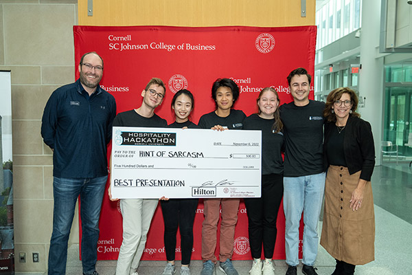 seven people standing in front of a red SC Johnson College of Business backdrop holding a large novelty check. 