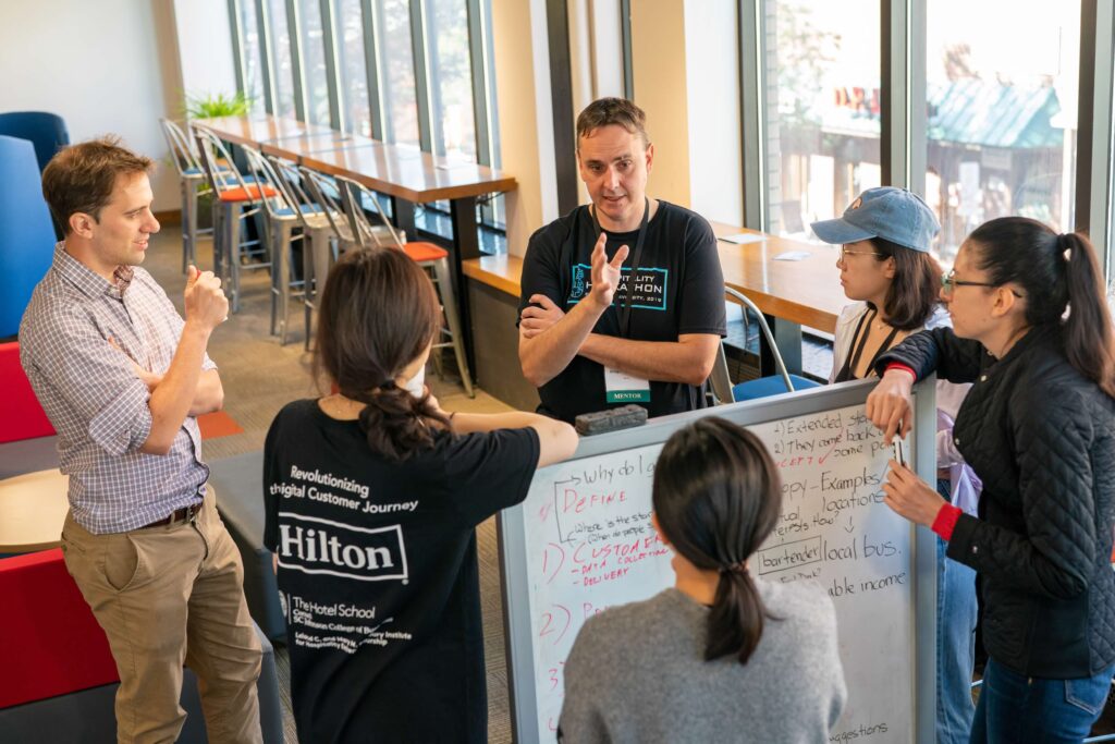 Rob Gregor '00, JD '07, founder and owner of Gregor Hotels, confers with Stefan Hench, MMH '20, Yi Xuan Huang, MMH '20, Kana Suda, MMH '20, Paulina Endara, MS '21, and Frances Wang, MS '21, during the 2019 Hilton Hospitality Hackathon. Their team, Sticky Notes, won the competition.