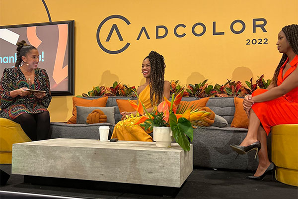 3 women seated on chairs and a couch the "ADCOLOR" signage behind them.