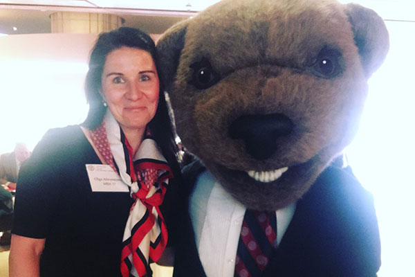 a woman smiling and standing close toCornell's mascot, a bear, wearing a business suit.