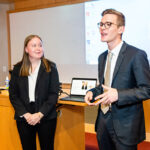 a young woman and man in business suits standing and delivering their presentation.