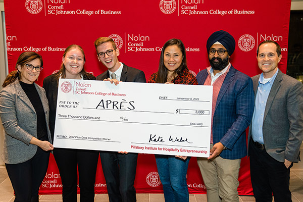 six people standing in front of a red SC Johnson College of Business backdrop holding a large novelty check. 