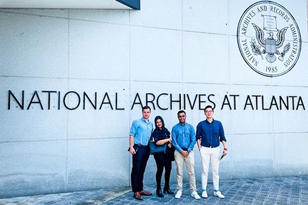 3 young men and 1 woman posing in front of a building with the National Archives sign and logo.
