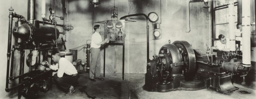 Students study machinery in an engineering lab, probably in the basement of Roberts Hall.