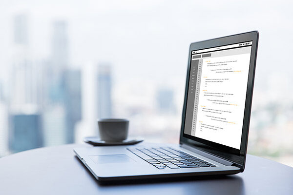 a laptop sitting on a desk with a coffee cup next to it, blurred buildings in the background.
