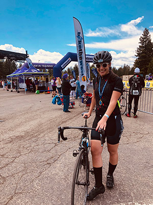 Mariam Kalandarishvili in a biking outfit standin and holding her bicycle with the finish line in the background.