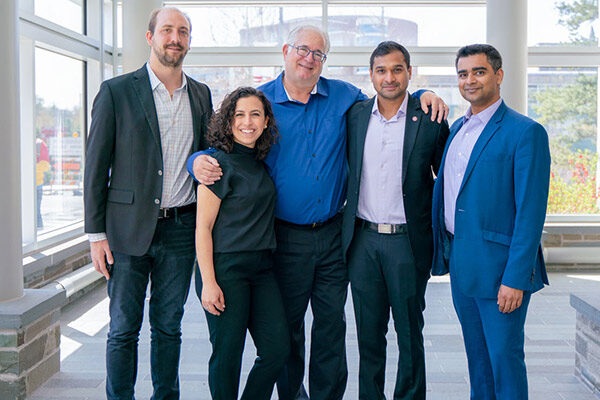 4 men and one woman standing and smiling.