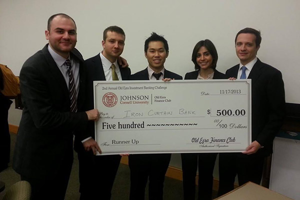 4 men and 1 woman in business suits holding a novelty check for $500.