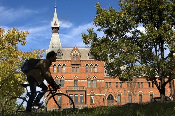 A student rides a bike with Sage hall in the background.