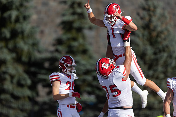 3 Cornell football players; one is hoisting Jameson up in the air.