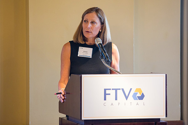 a woman in a black dress standing and speaking at a podium.