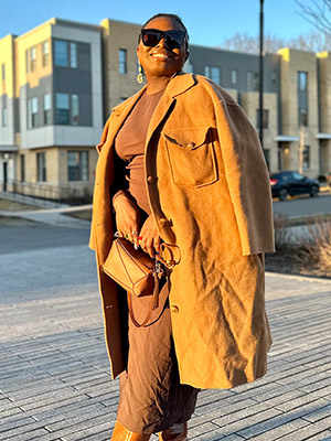 Kafilatu Tiamiyu dressed in business attire and smiling, standing on a sunny street.