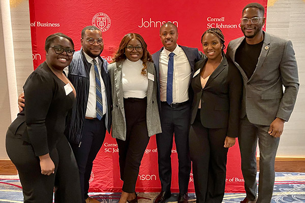 3 black women and 3 black men, dressed in business attire, smiling and standing in front of a Johnson / SC Johnson College of Business backdrop.