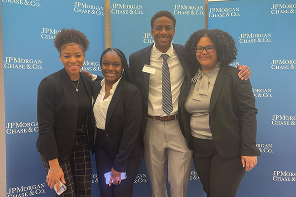 Melanie Abreu with 3 other people dressed in business attire, standing in front of a JP Morgan Chase & Co. backdrop.