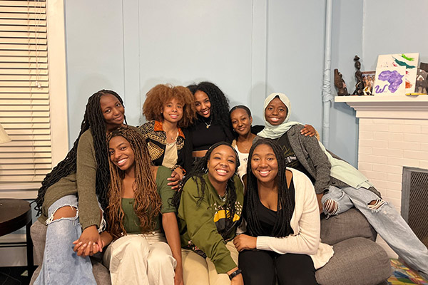 eight young Black women clustered together on a couch and smiling.