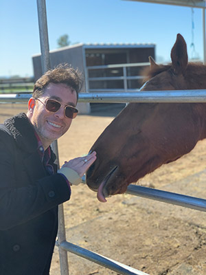 a smiling man standing and petting the nose of a horse.