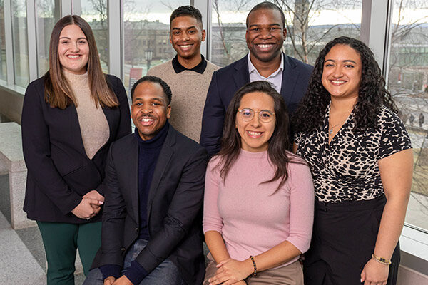 3 men and 3 women dressed in business casual posing in front of a window and smiling.