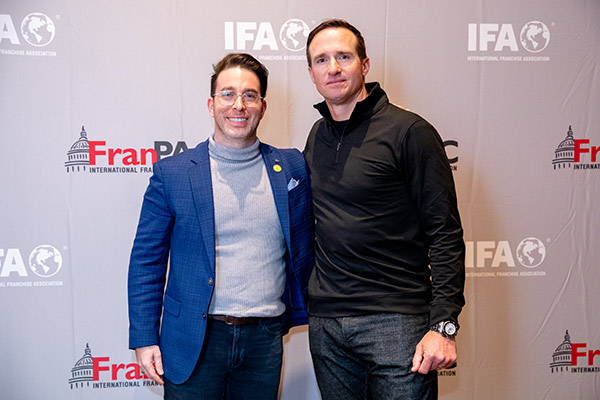 two men standing next to each other in front of a backdrop with the International Franchise Association logo.