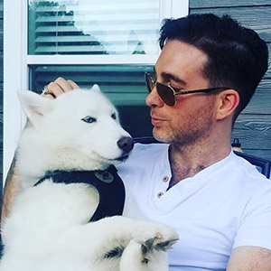 a man petting and looking at a large white dog sitting on his lap.