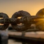 links of a large metal chain with the rising or setting sun shining through one of the links.