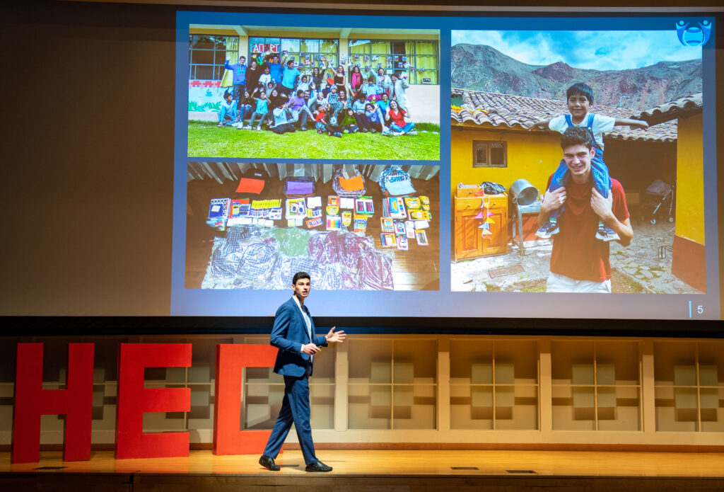 Lucas Suero presents his pitch on stage with a large screen behind him showing pictures of kids in Peru.