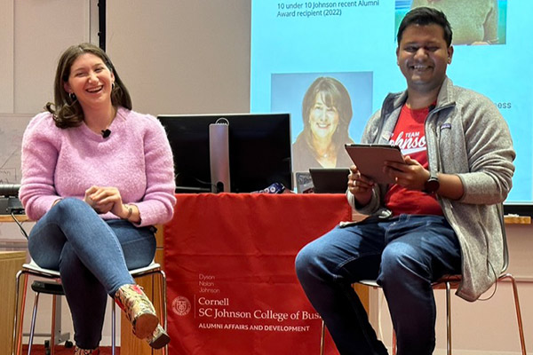 Danielle Boris and an interviewer sit side by side on stools with an SC Johnson College of Business banner draped over the podium/desk behind them.