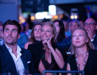 Three people in the audience watch the Nolan celebration video at the 2022 Gala.