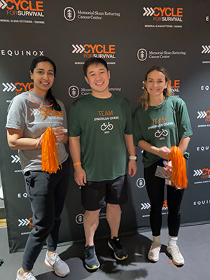 Samuel Cho and two women wearing cycling T-shirts posing in front of a Cycle for Survival / Memorial Sloan Kettering Cancer Center backdrop.