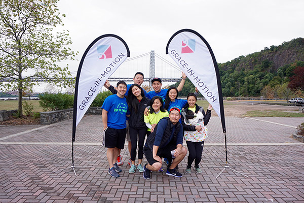 8 men and women in shorts and T-shirts holding up "Grace-In-Motion" banners that form an arch over them.