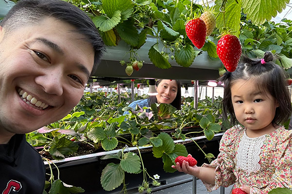 Samuel Cho, his toddler daughter, and his wife surrounded by strawberry plants growing in tiers of raised beds.