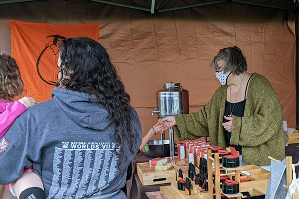 A woman behind a table with skincare products interacting with a customer.