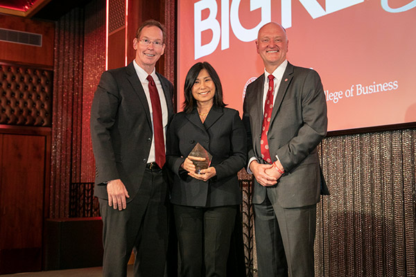 two men and a woman on stage, in business attire. 