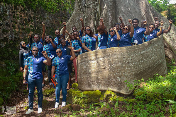 about 20 young people in matching blue T-shirts standing at the base of an enormous tree, left fists held high. 