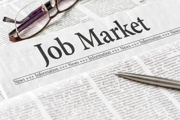 A newspaper with the headline Job Market, with glasses and a pen on top.