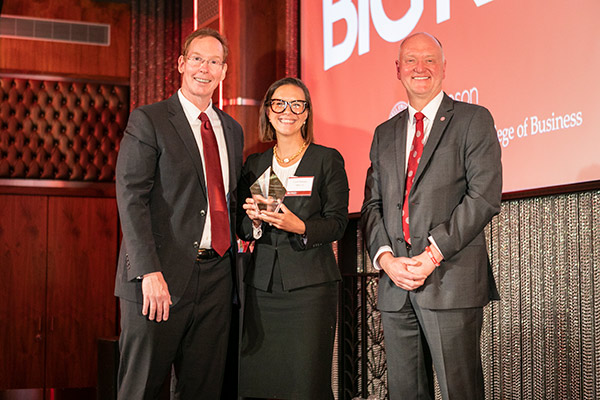 two men and a woman on stage, in business attire. 