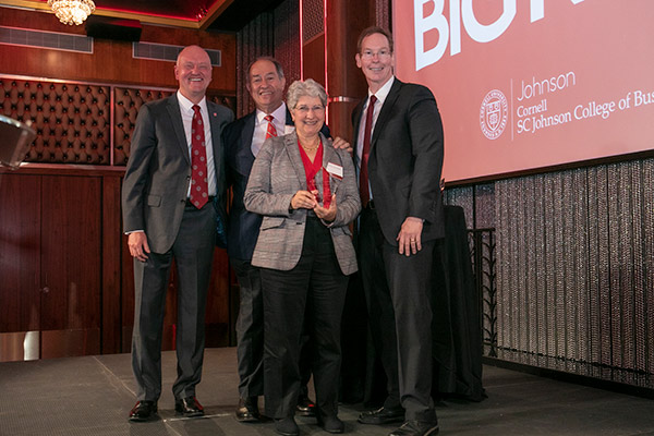 three men and a woman on stage, in business attire. 