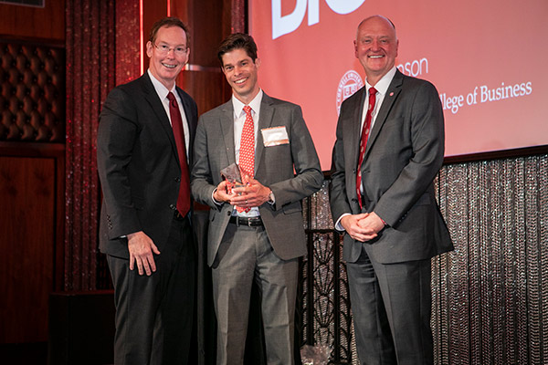 three men on stage, in business attire. 