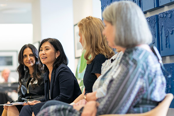 Angela Hwang leaning forward and speaking with other panelists seated beside her.