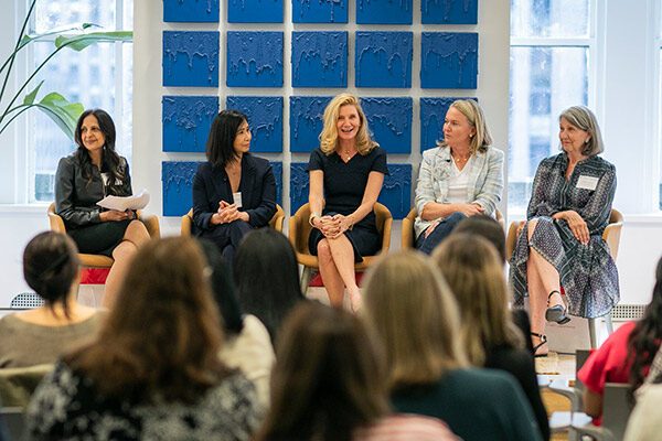 5 women sitting on a low, platform stage with the heads of the audience in the foreground.