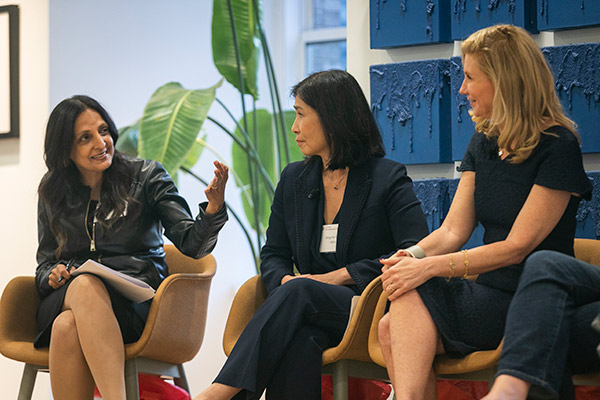 Rainu Kaushal gestures with her hand in the air while speaking to two woman panelists pictured and seated beside her. 