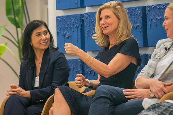 Holly Sheffield gestures with one hand in the air with two woman panelists seated on either side of her.