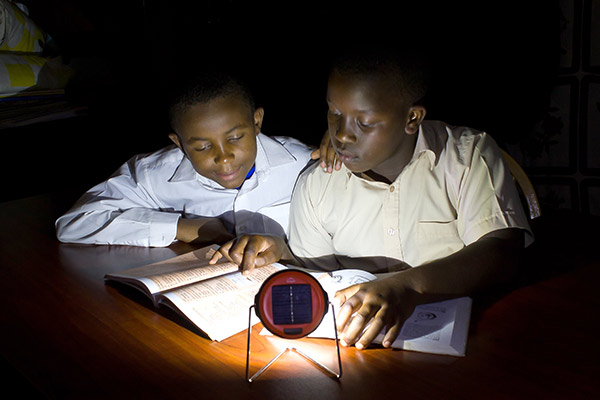 Two boys sitting at a desk at night and studying in a pool of light provided by a lantern on the desk.