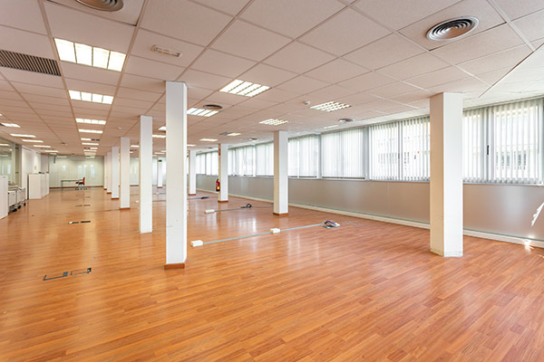 photo of an empty room with outlets and cable boxes built into the wood floor and windows along one side.