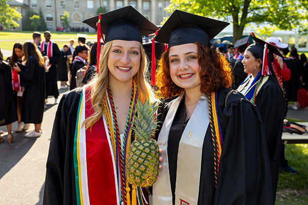 Two women in graduation caps and gowns on the Cornell Arts Quad. 