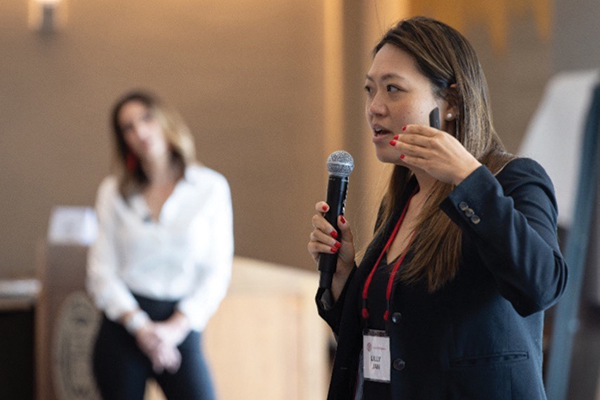 Lilly Jan speaks into a microphone while another speaker looks on.