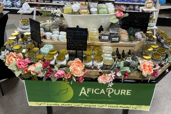 A wooden table with a display of skincare products arranged on it with a large sign in green that reads AficaPure. 